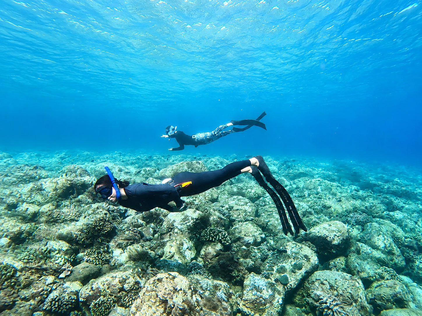 Two women underwater freediving on top of a coral reef in Bali